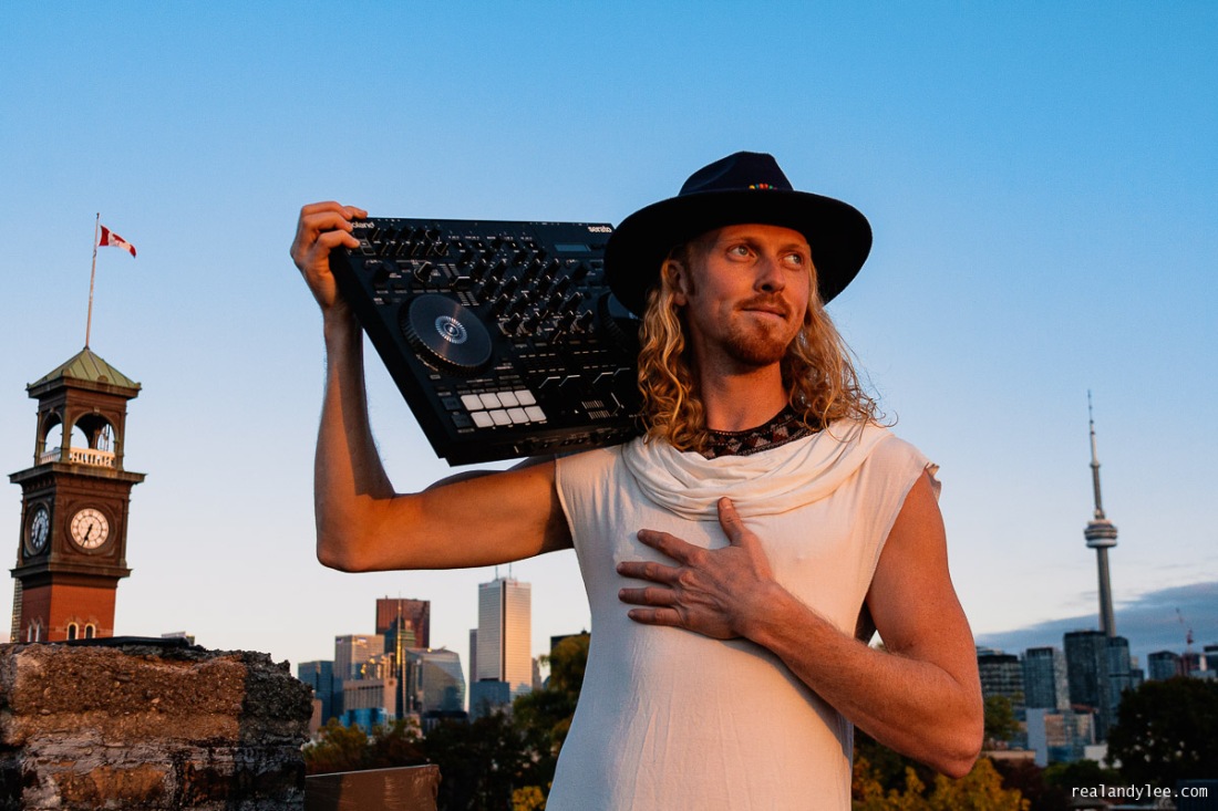 Jesse Buck holding a mixer and his hand over his heart with the Toronto skyline in the background. © Andy Lee, realandylee.com